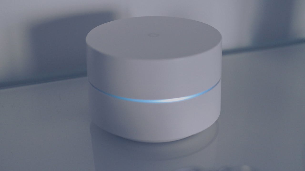 A clean and modern minimalist design of a white round electronic device with a blue light ring on a reflective glass surface.